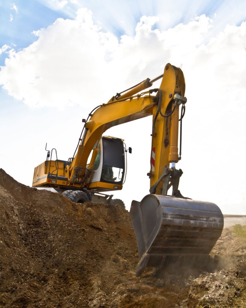 A yellow excavator dragging dirt up a steep bank.